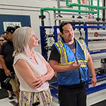 Tyrone Starr and Minister Hajdu stand in front of 2 reporters with cameras, touring the water treatment plant.