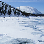 A photograph by Christophe Migeon capturing a Nunavik landscape where fractured ice spreads across a stretch of water.